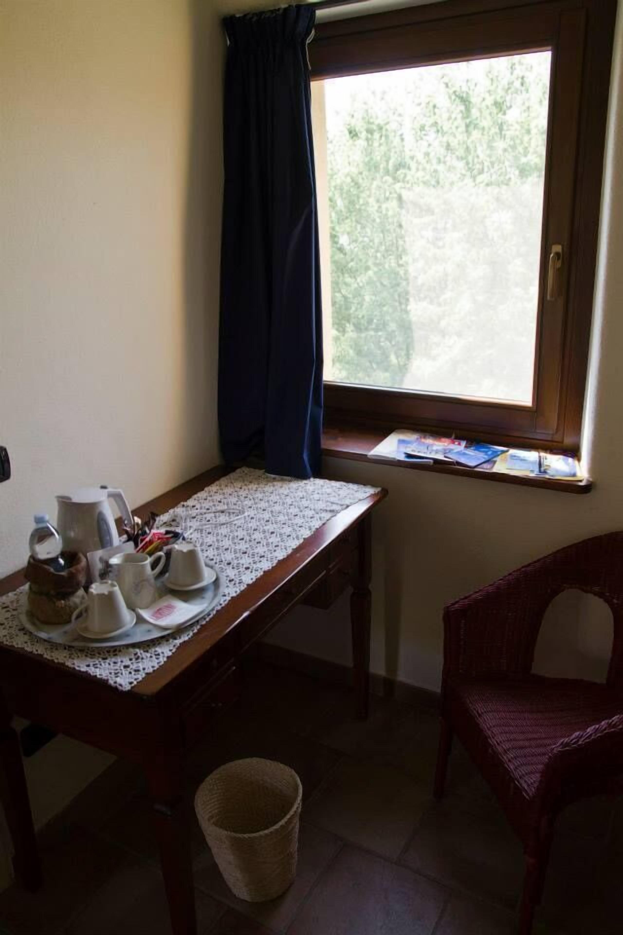 A small room with a table set for breakfast, a wicker chair, a window with curtains, and a basket on the floor.