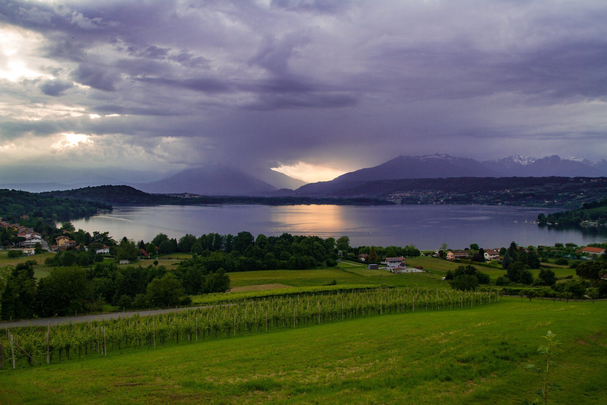Ein weiter Panoramablick auf einen See, umgeben von grüner Landschaft und einem Berg im Hintergrund.