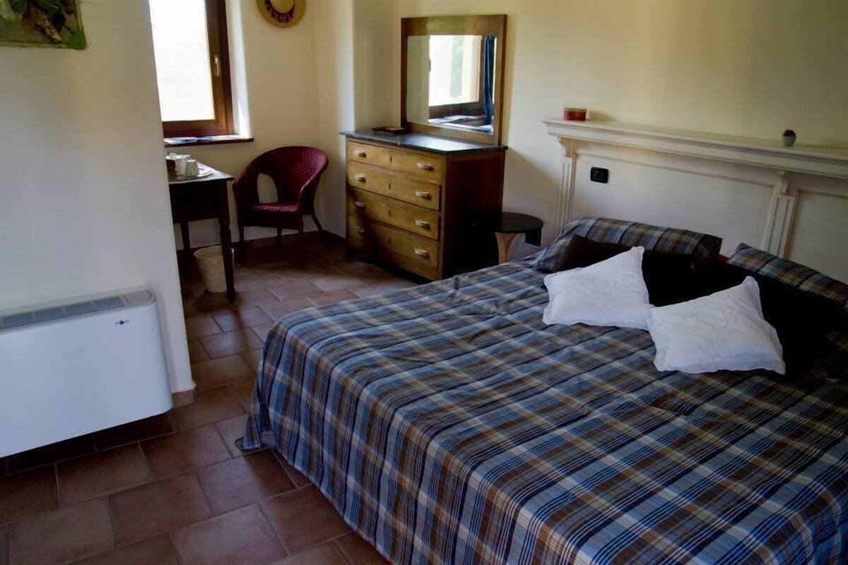 Een slaapkamer met een bed, een kapstok, een stoel en een radiator.