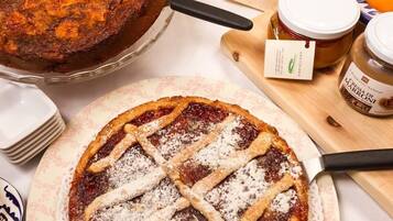 Un tavolo imbandito con dolci, una torta, una crostata, pane e barattoli di marmellata.