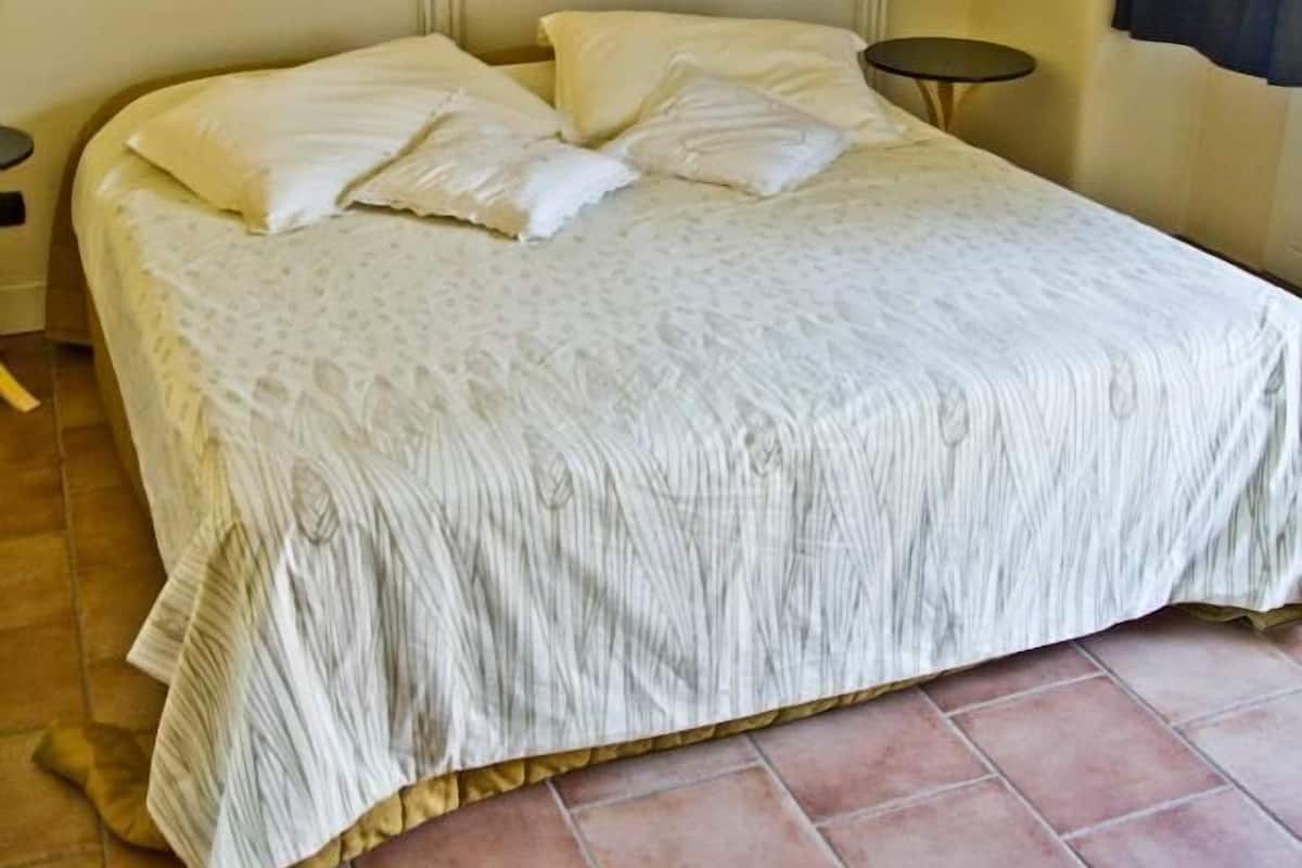 Een bed met een beddekleed met patroon, een nachtkastje en een wandlamp.