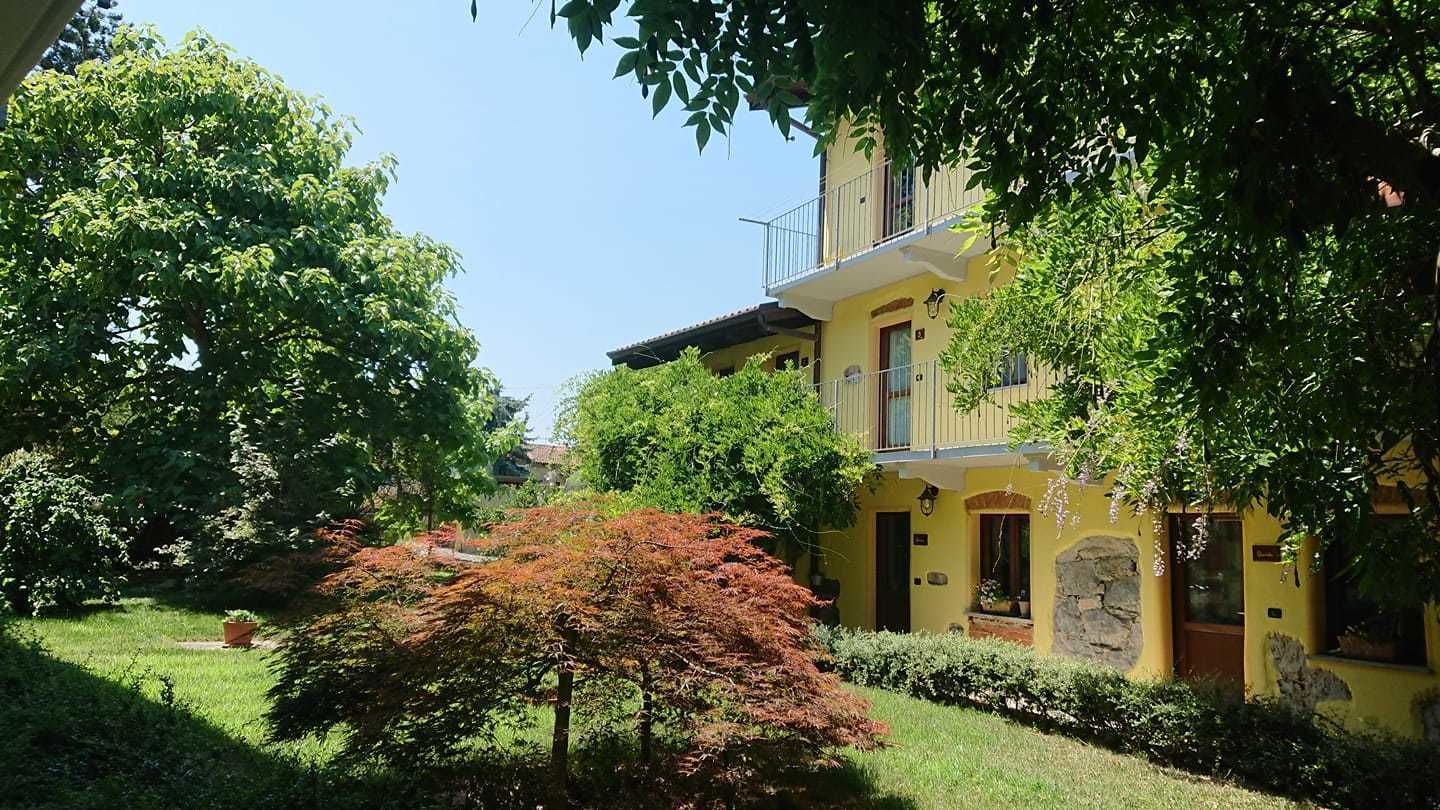 A yellow building with a balcony, surrounded by lush greenery and trees.