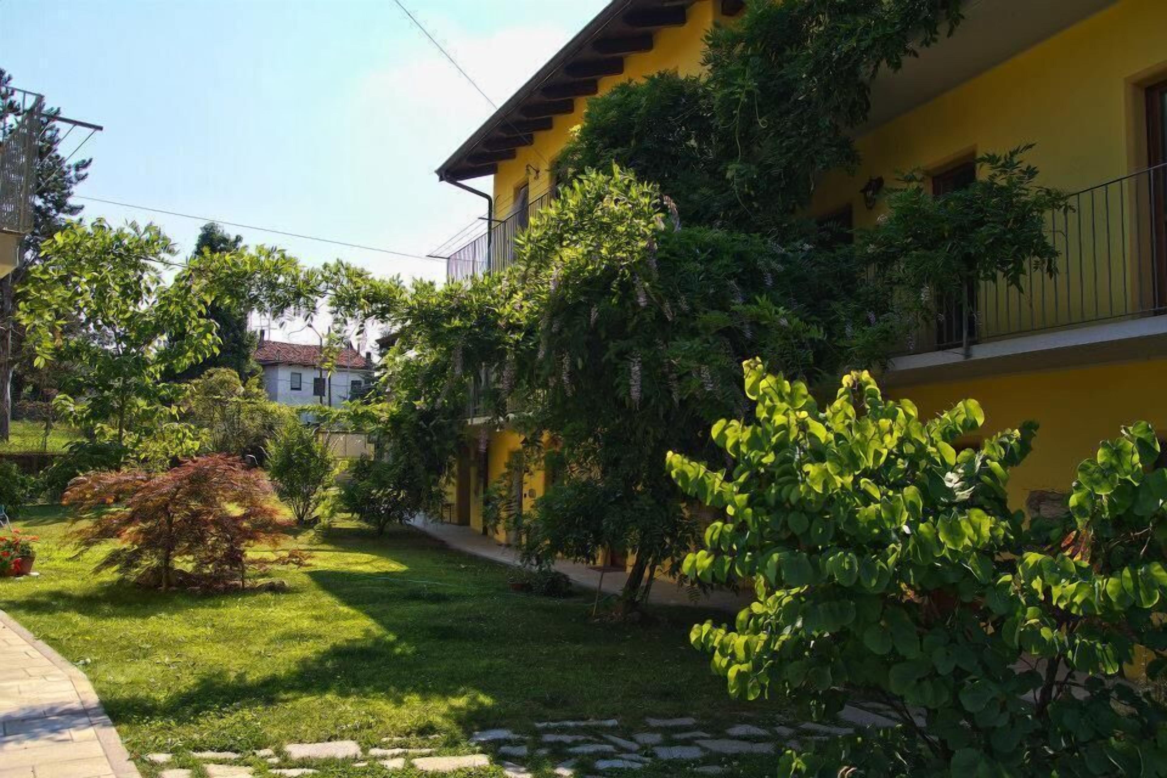 Um edifício amarelo com varanda, rodeado por vegetação e um caminho de pedra.