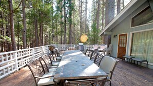 A wooden deck with a long table and chairs, surrounded by a white fence and tall trees. - The Tree House II (Yosemite National Park)