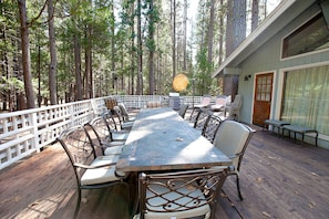 A covered outdoor dining area with a long table and chairs, surrounded by a white fence, set in a forested area. - The Tree House II (Yosemite National Park)