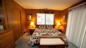 A bedroom with a wooden floor, a bed with a quilt, two bedside lamps, a bench, a wooden dresser, and a window with blinds. - The Tree House II (Yosemite National Park)