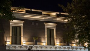 Un edificio con balcón, ventanas amplias y fachada iluminada en la noche.