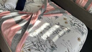 Habitación de hotel con dos camas, cada una con ropa de cama floral y un cojín con diseño de canguro. Se observan toallas enrolladas sobre las camas y una mesita de noche con un control remoto.