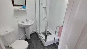 Baño con inodoro, lavamanos y ducha con mampara de vidrio.