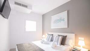Habitación de hotel con cama, televisor montado en la pared, ventana y un cuadro en la pared.