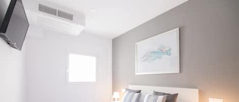 Une chambre d’hôtel avec un lit, un téléviseur fixé au mur, une fenêtre et un tableau accroché au mur.