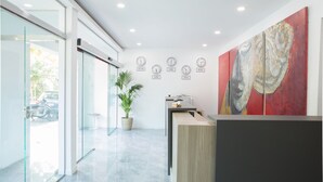 Zona de recepción con puerta de vidrio, mostrador de recepción, planta en maceta y un cuadro abstracto grande en la pared.