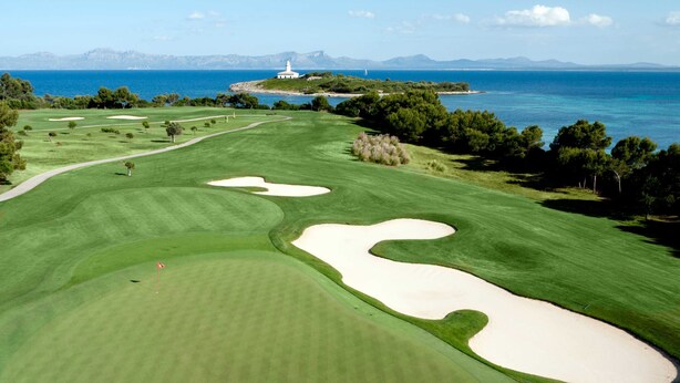 Un campo de golf con búnkeres, un faro y vistas al mar y a las montañas.