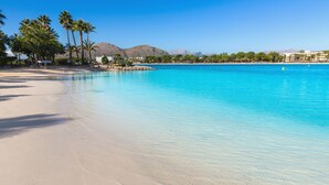 Una playa con agua turquesa cristalina, palmeras y montañas al fondo.