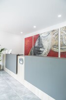 Un mostrador de recepción de diseño moderno, un cuadro abstracto grande en la pared y una planta en maceta a la izquierda.