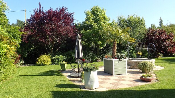 Un giardino curato con un patio, una zona salotto e diverse piante e alberi.