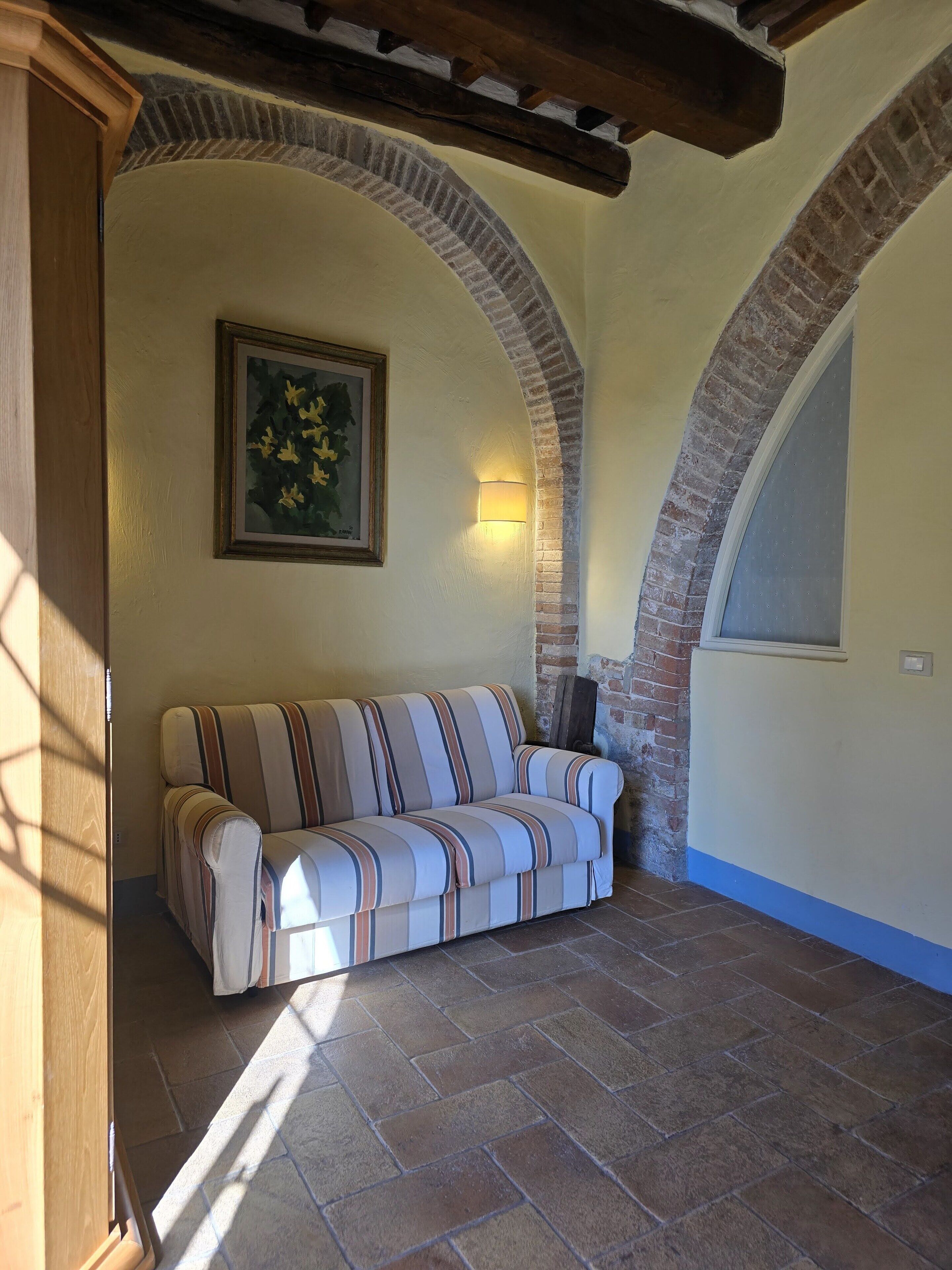 Una habitación acogedora con un sofá a rayas, un cuadro en la pared y un arco de ladrillo.
