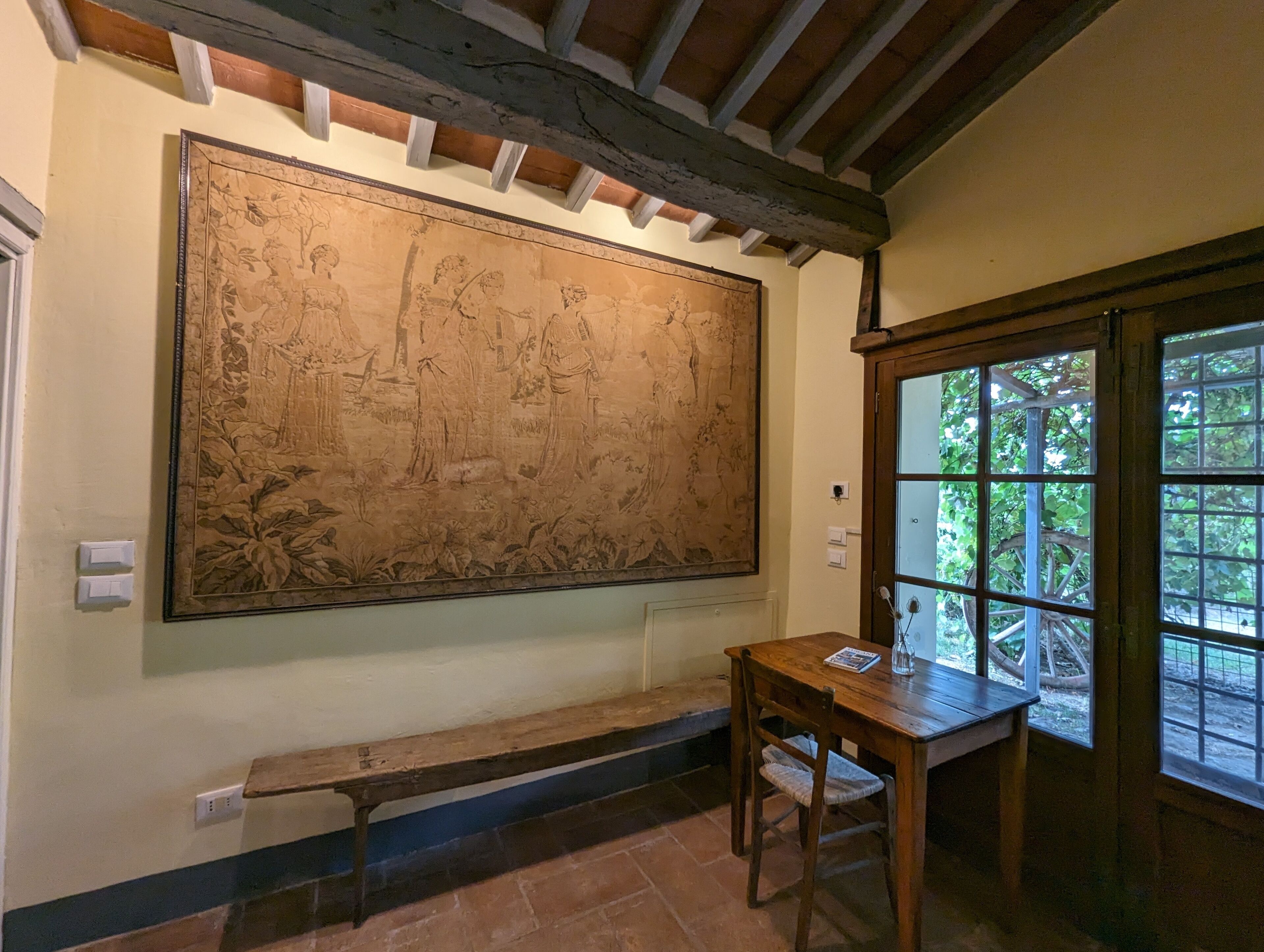 A room with a large mural, a wooden bench, a table, and a window with a view of greenery.