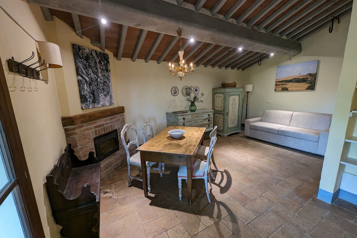 A dining area with a wooden table, chairs, a fireplace, a chandelier, and a sofa.