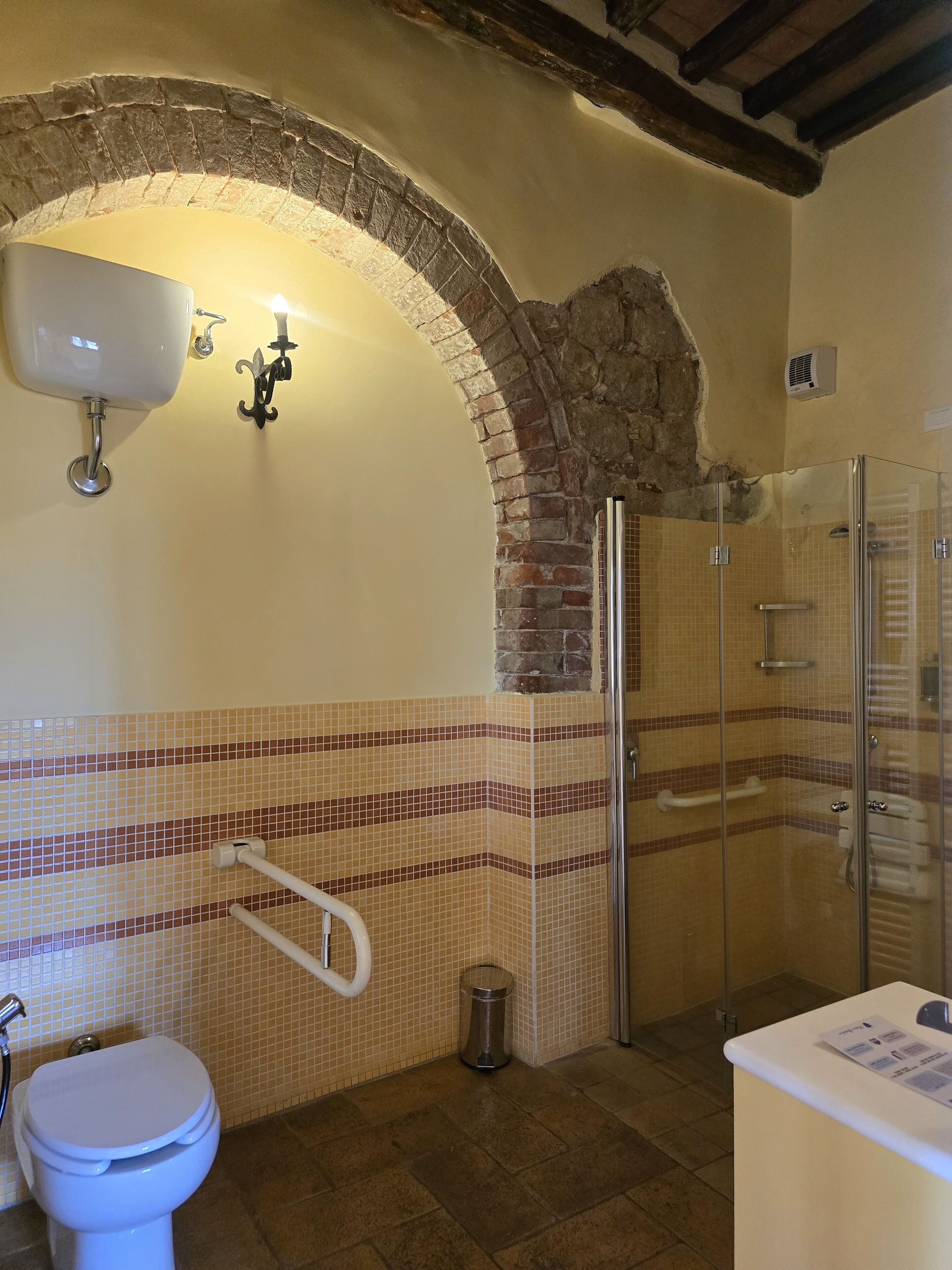 Un baño con pared de azulejos, ducha, inodoro y lavamanos.