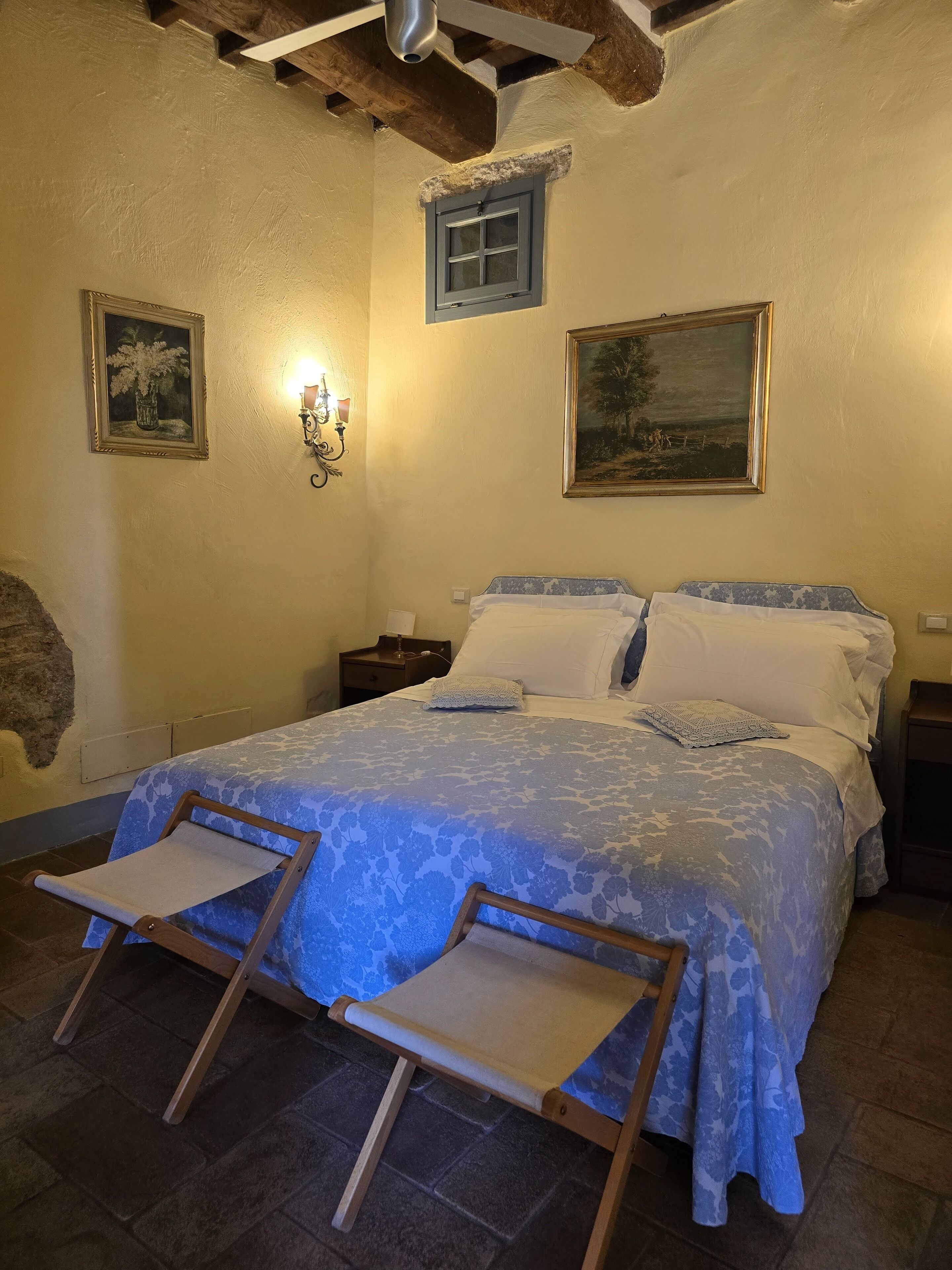 A bedroom with a bed, two nightstands, a wall-mounted lamp, and two framed pictures.