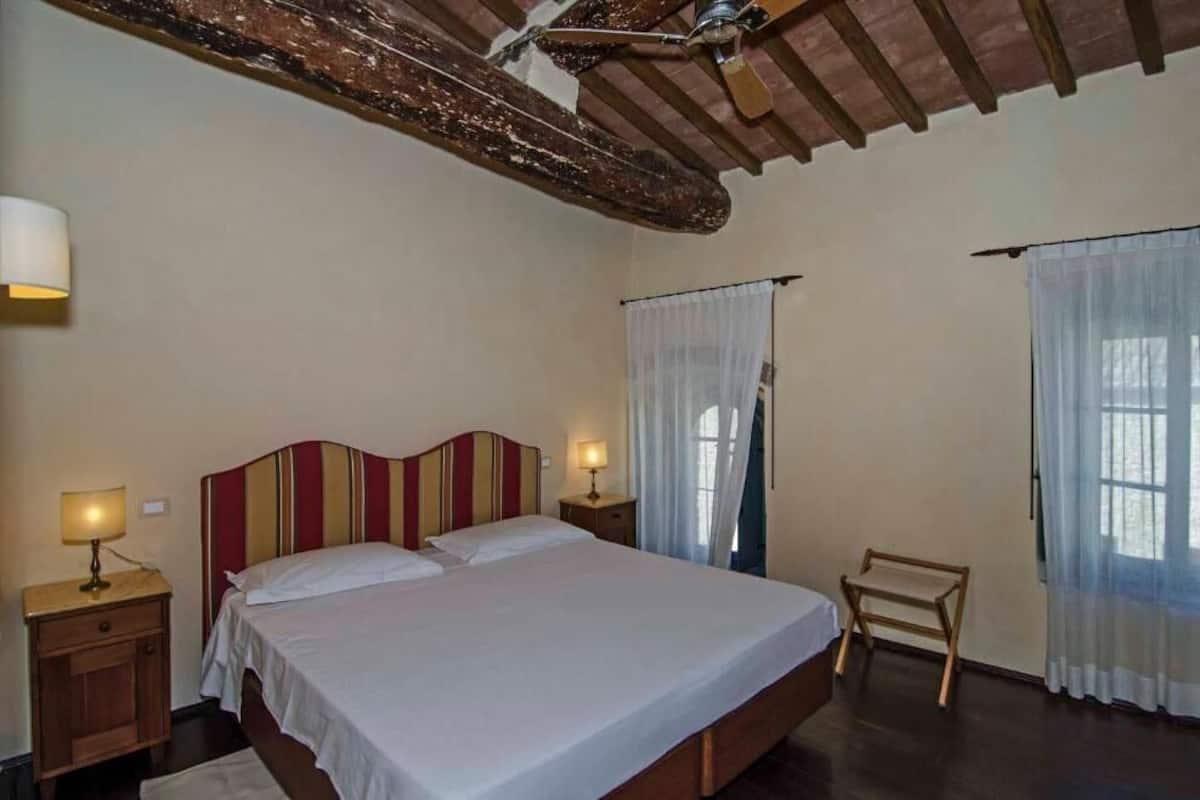 A bedroom with a wooden headboard, a bed with white linens, two bedside lamps, a wooden bench, and a ceiling fan.