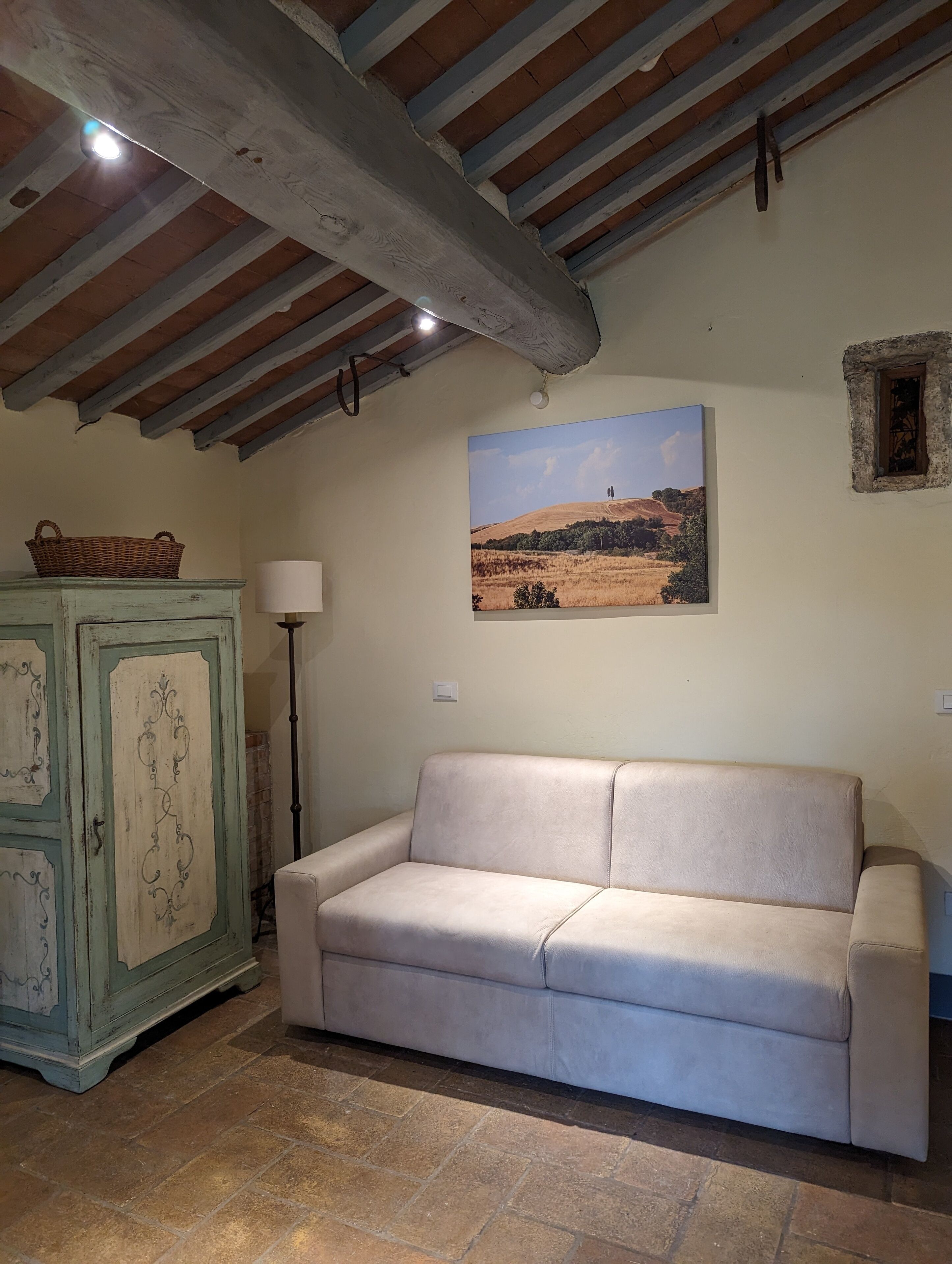 Une pièce avec un canapé beige, un meuble vert et un tableau représentant un paysage.