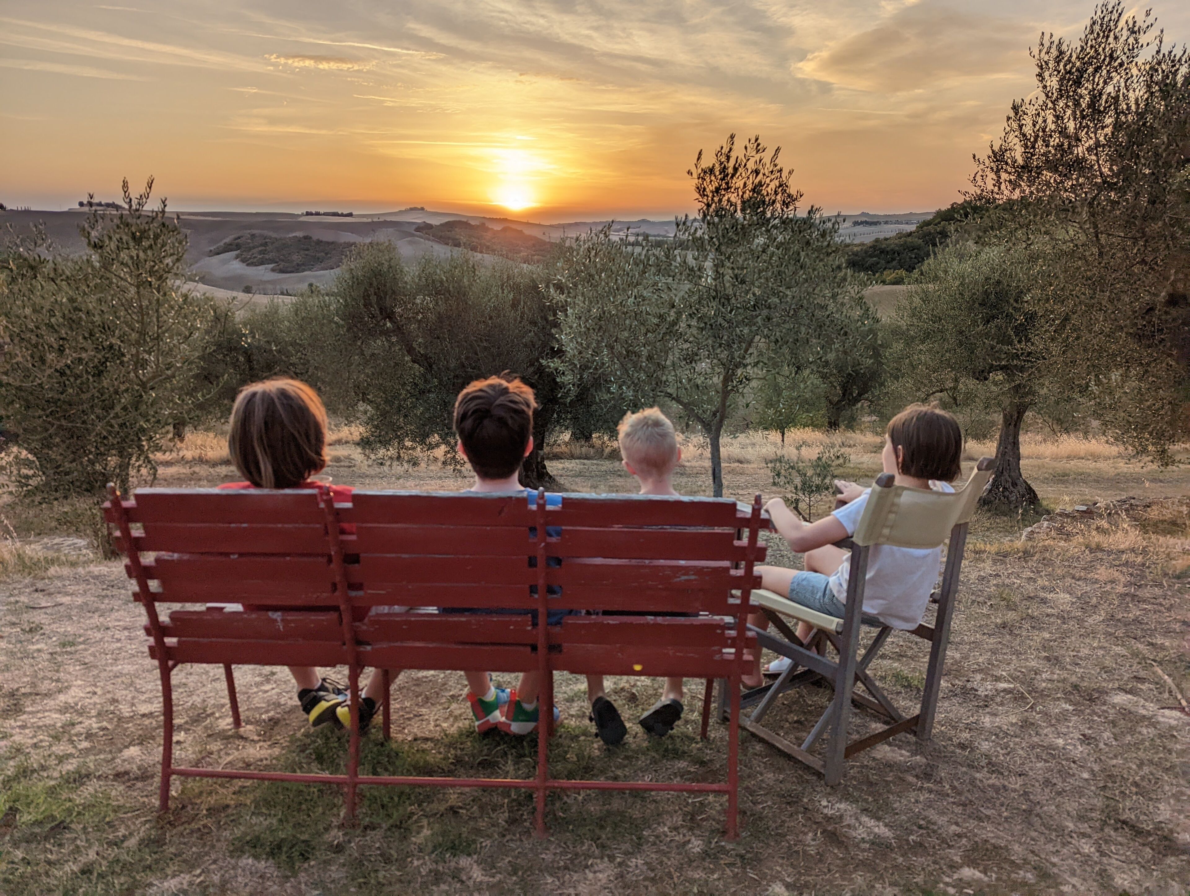 Trois personnes sont assises sur un banc, face à un coucher de soleil.