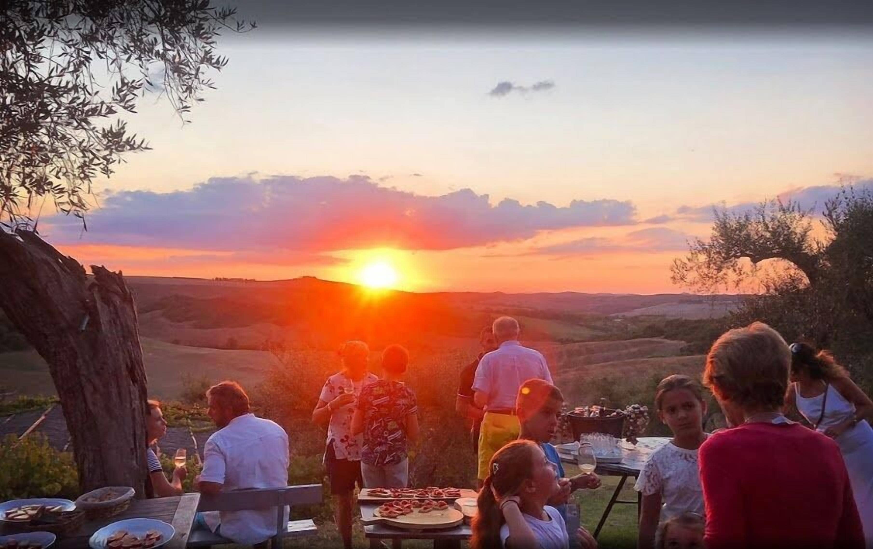 A group of people dining outdoors at sunset with a view of the landscape.
