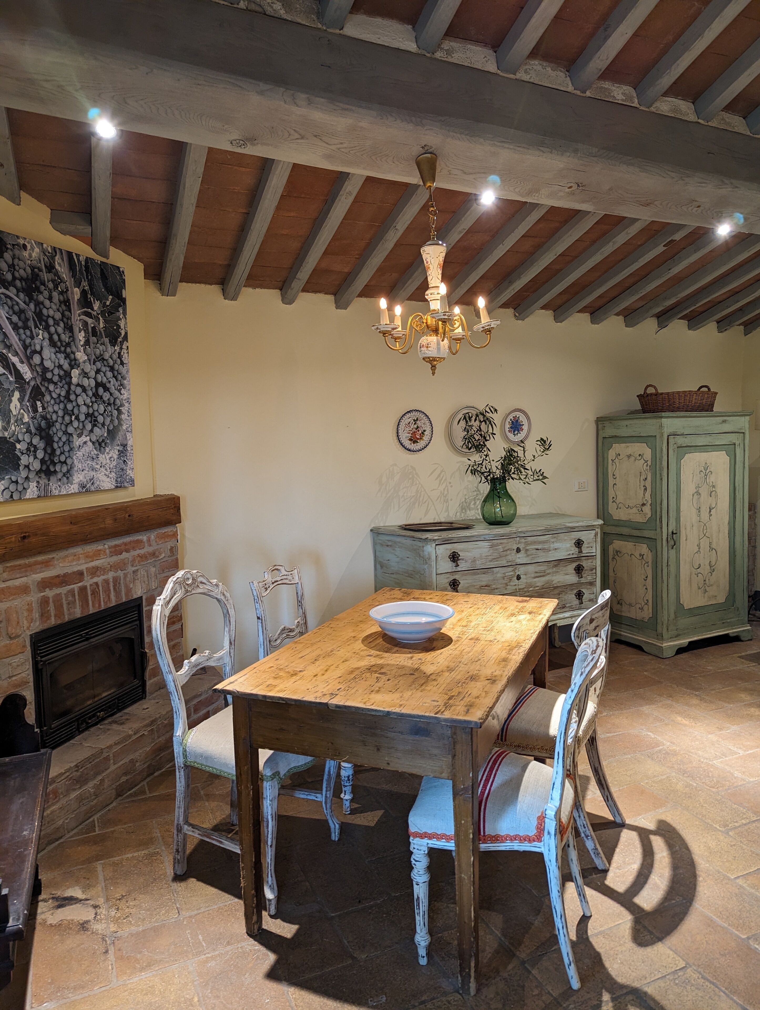 A rustic dining area with a wooden table, white chairs, a chandelier, and a fireplace.