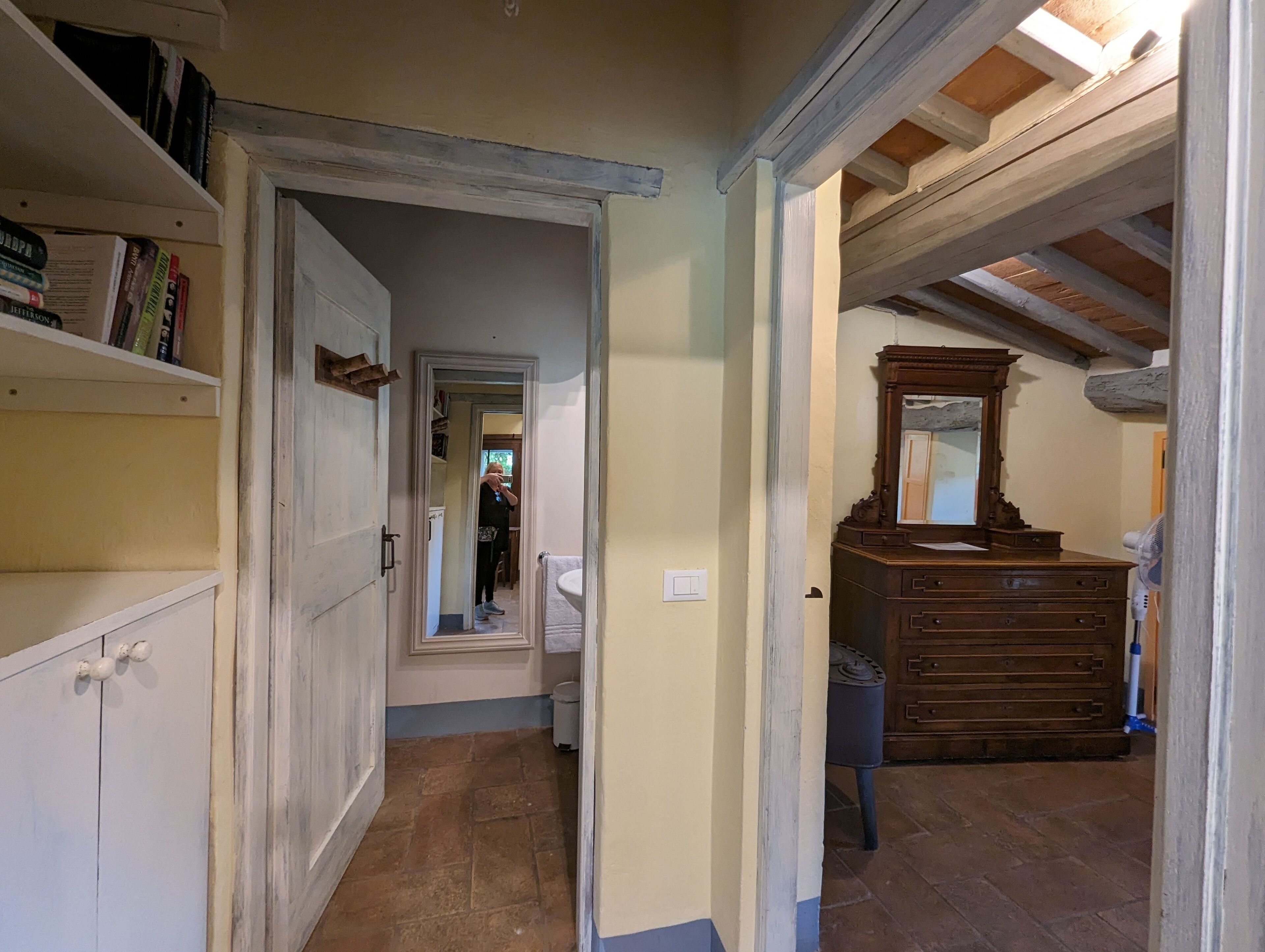 A narrow hallway with a wooden dresser and a mirror. A door leads to another room.