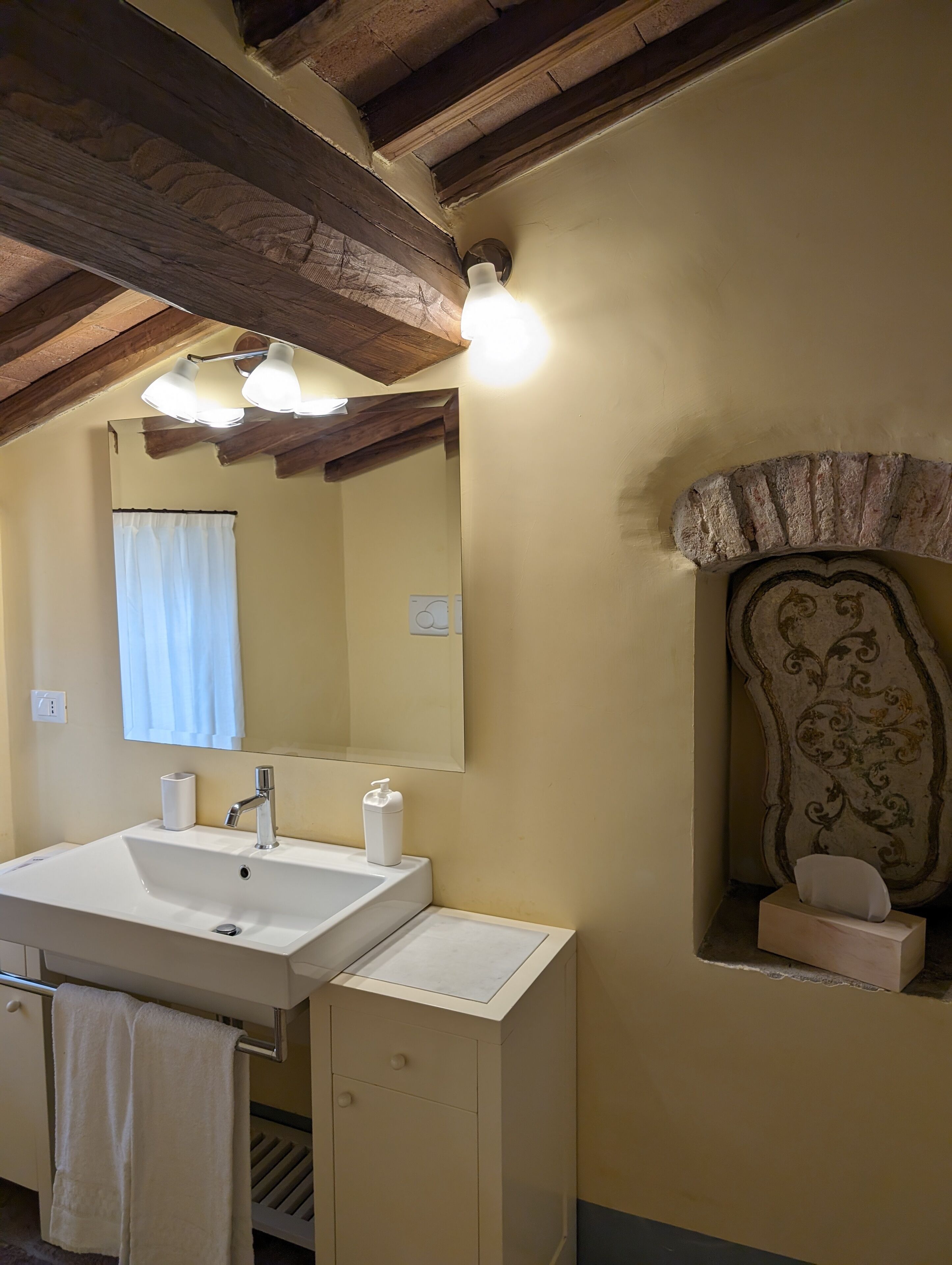 Un baño con un lavamanos blanco, un espejo, un perchero para toallas y un arco decorativo en la pared.