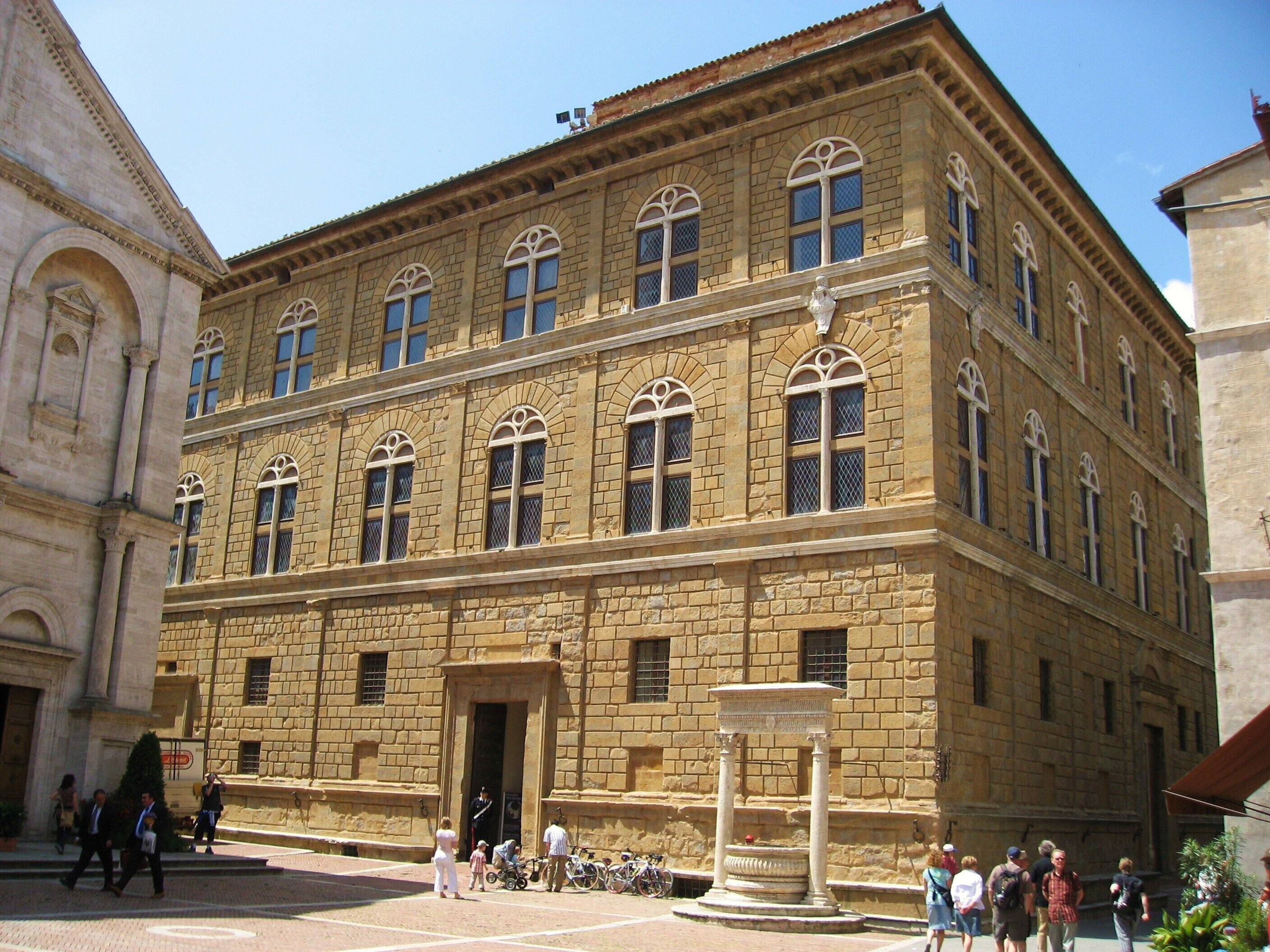 A historic building with a central entrance, large windows, and a fountain in the courtyard.