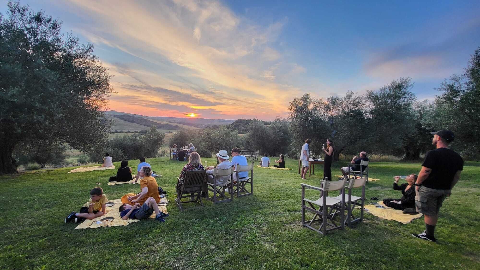 Un grupo de personas disfruta de un picnic en un espacio abierto con césped y vistas espectaculares al atardecer.