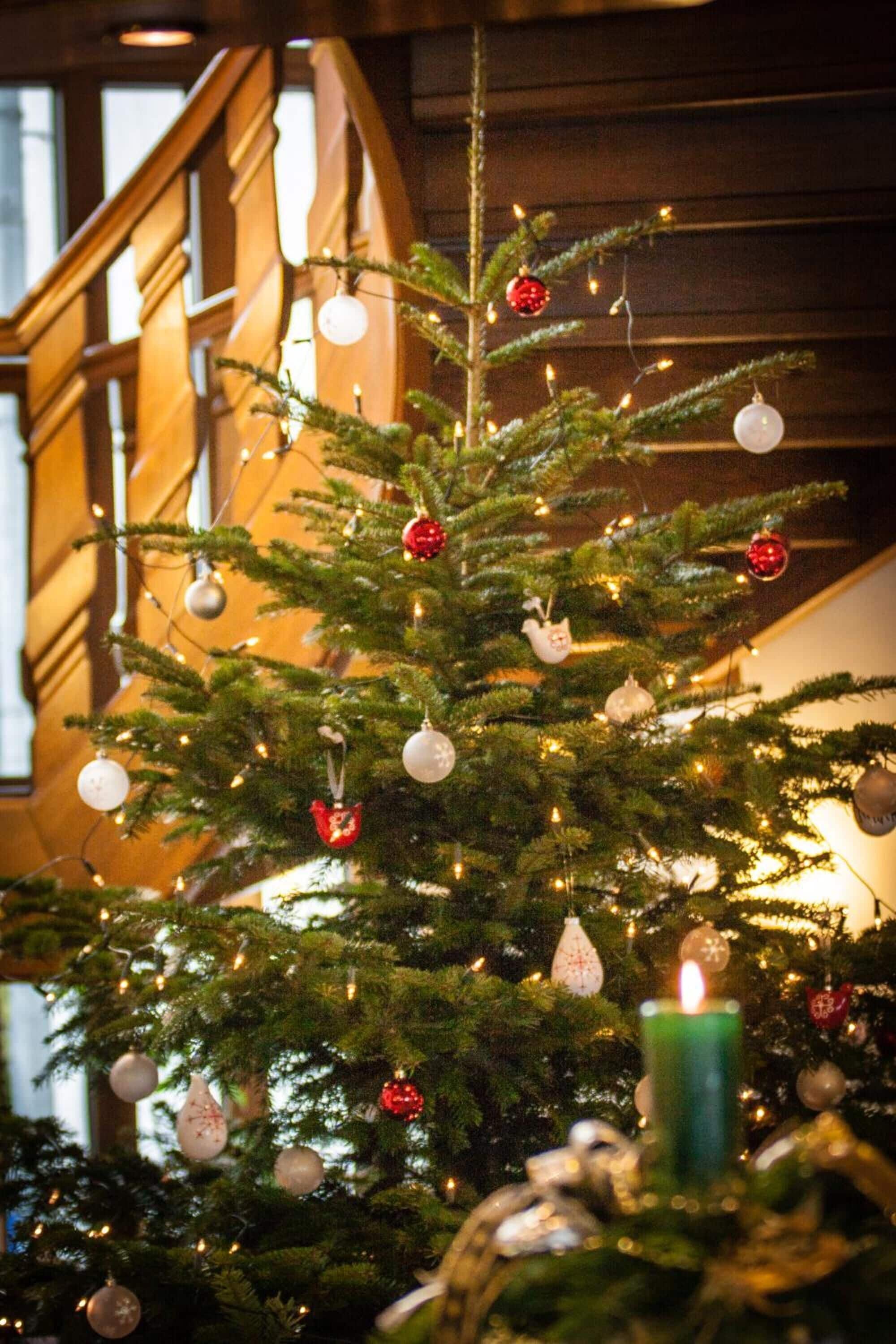 A Christmas tree with ornaments and lights, a green candle, and a staircase in the background.