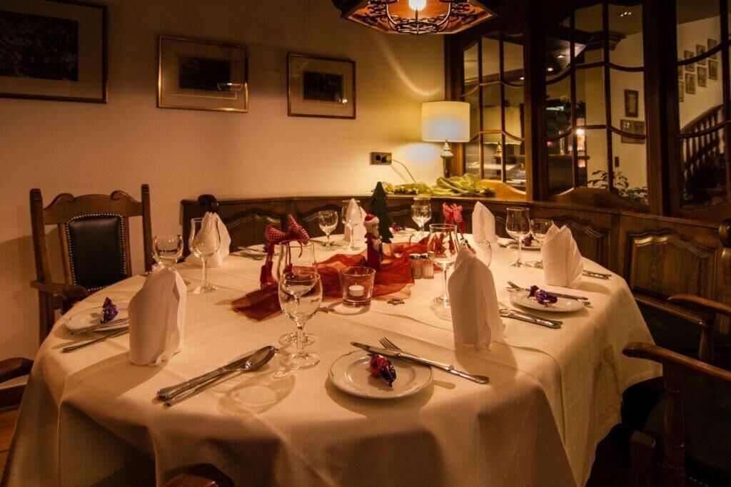 Een eettafel gedekt met een witte tafelkleed, borden, bestek en wijnglazen, met een kroonluchter erboven.