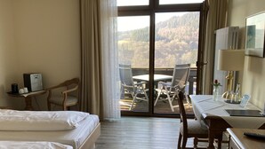 A hotel room with two beds, a desk, a chair, a small table with a coffee maker, and a view of a deck with outdoor furniture. - Hotel Landhaus Müllenborn (Gerolstein)