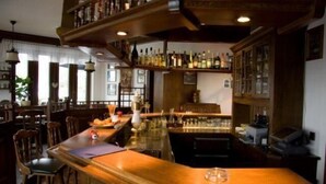 A bar area with wooden bar counters, shelves with bottles, and a seating area with chairs. - Hotel Landhaus Müllenborn (Gerolstein)