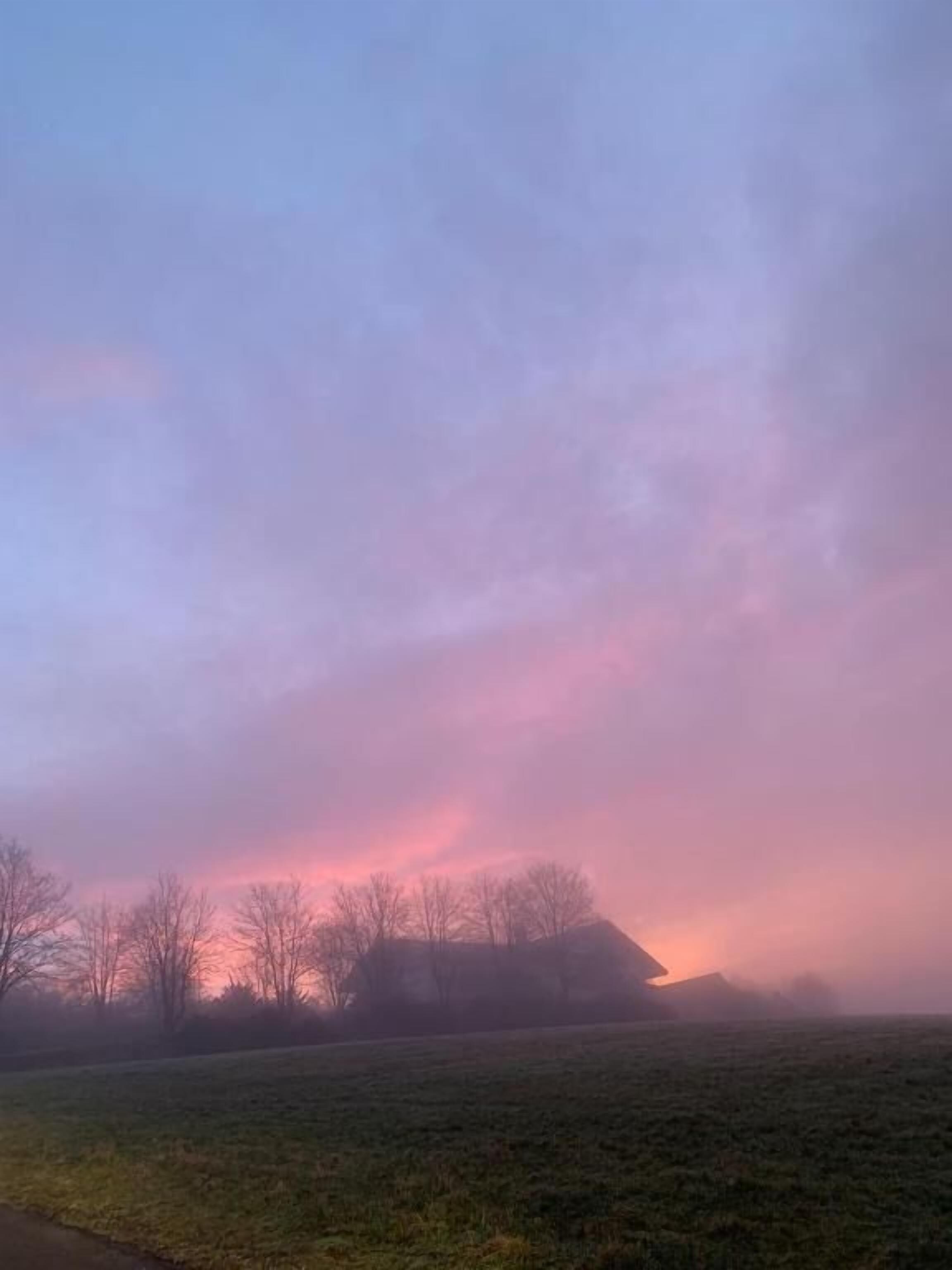 Paesaggio rurale con un campo pianeggiante, qualche albero e un edificio in lontananza.