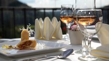 A table with a dessert, two wine glasses, and a spoon on a terrace with a view.