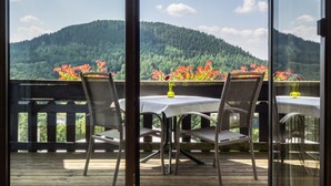 A balcony with a table and chairs, overlooking a forested mountain. - Hotel Landhaus Müllenborn (Gerolstein)
