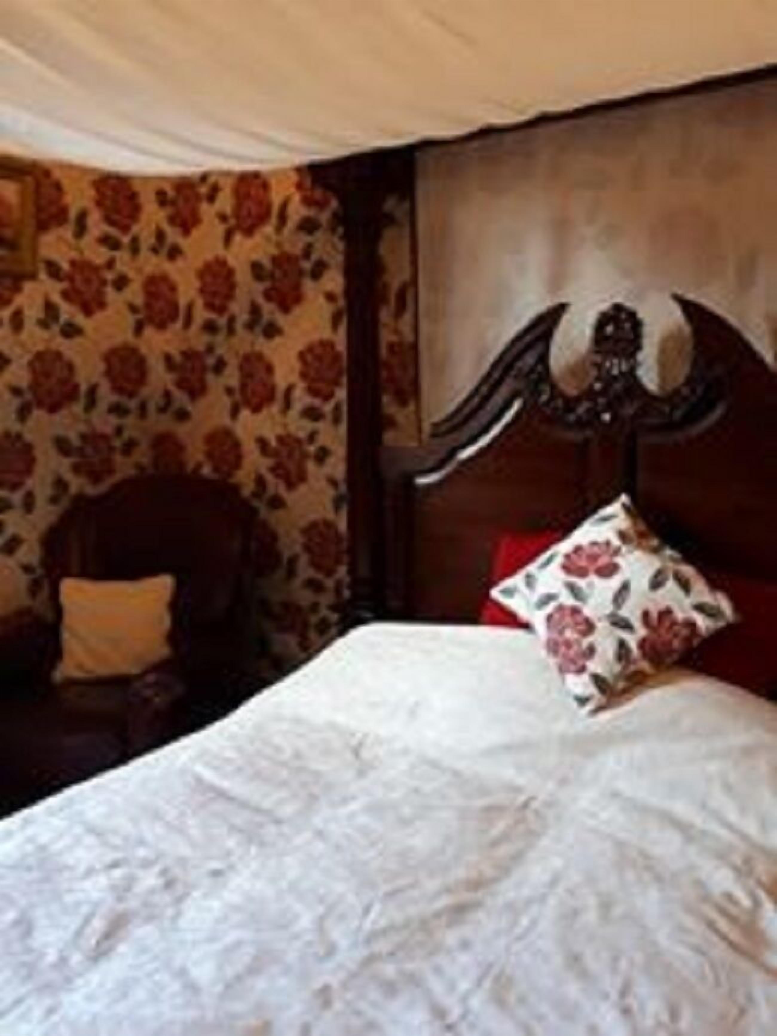 A bedroom with a bed, floral wallpaper, a wooden headboard, and a chair with a cushion.