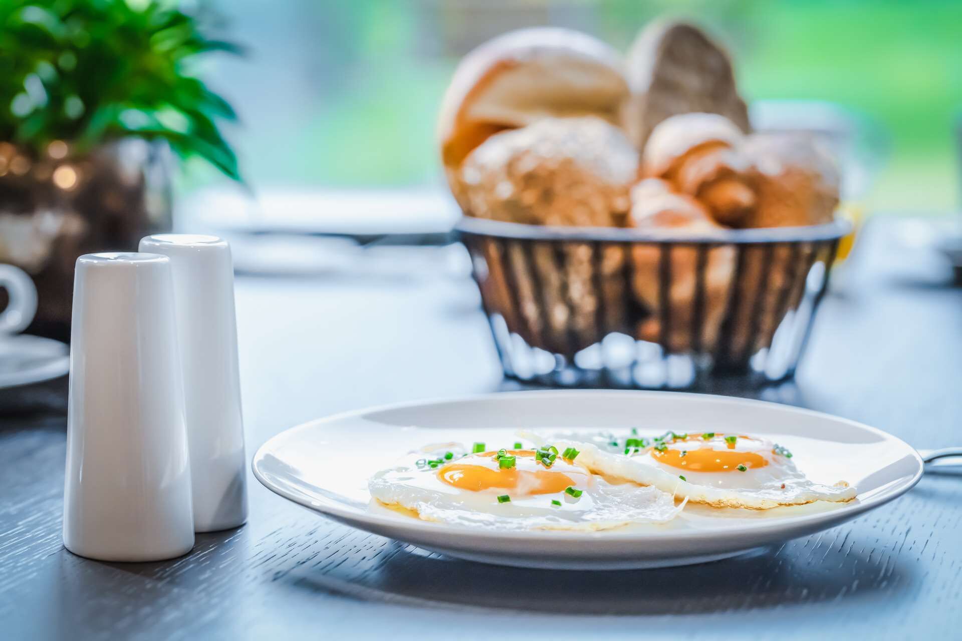 Une table mise pour le petit-déjeuner avec une assiette d’œufs au plat, des salières et des poivrières, et un panier de pain.