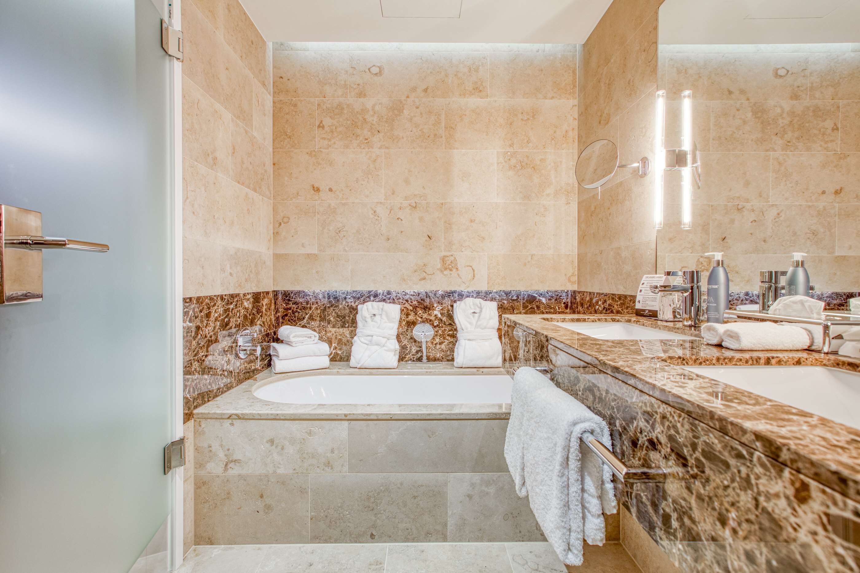 Un baño moderno con una bañera grande, dos lavamanos y un tocador con espejo.