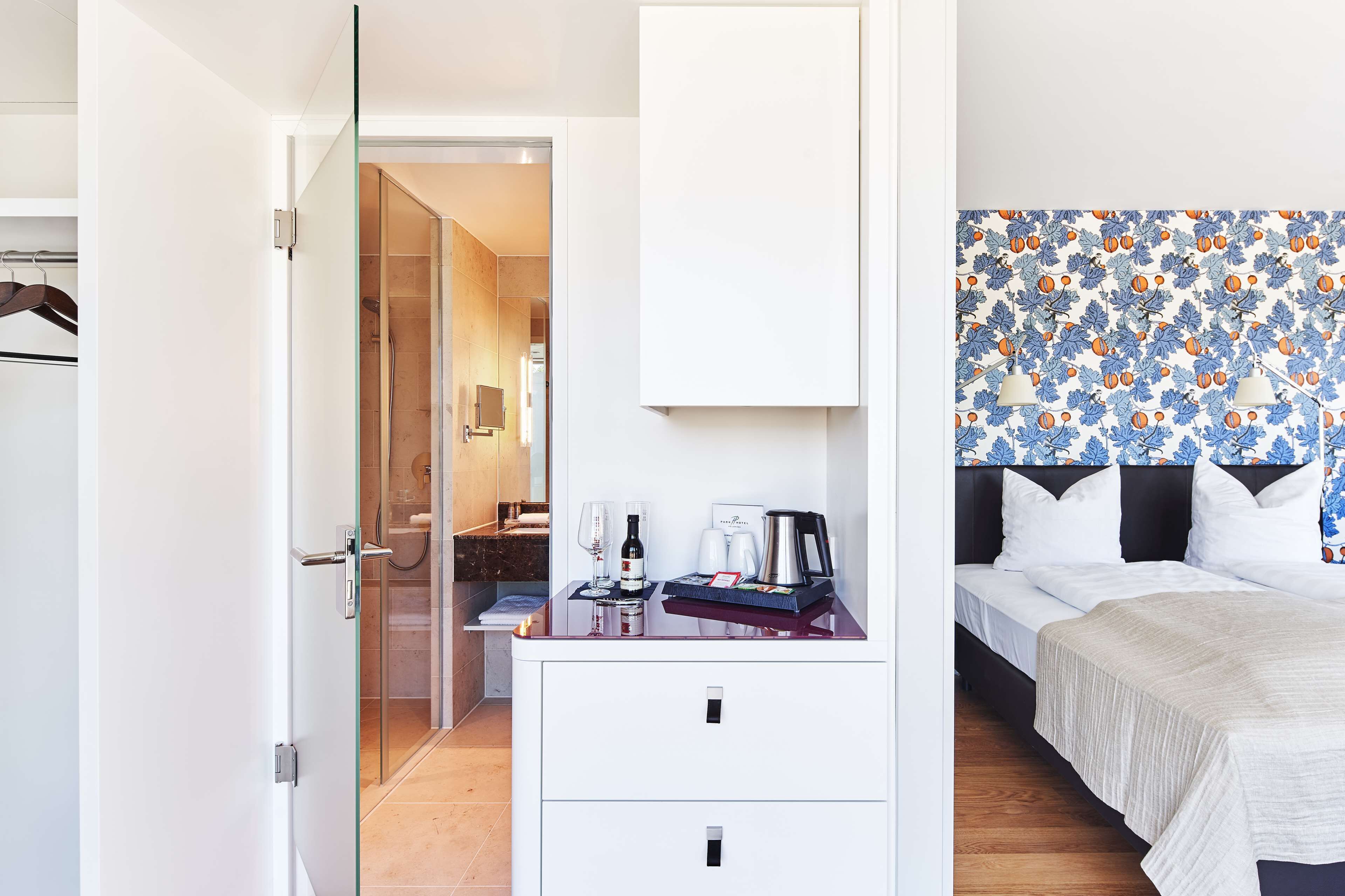 A hotel room with a bed, a desk with a coffee maker, and a shower area.