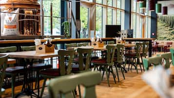 A restaurant interior with wooden tables and chairs, a large copper brewing apparatus, and large windows allowing natural light.