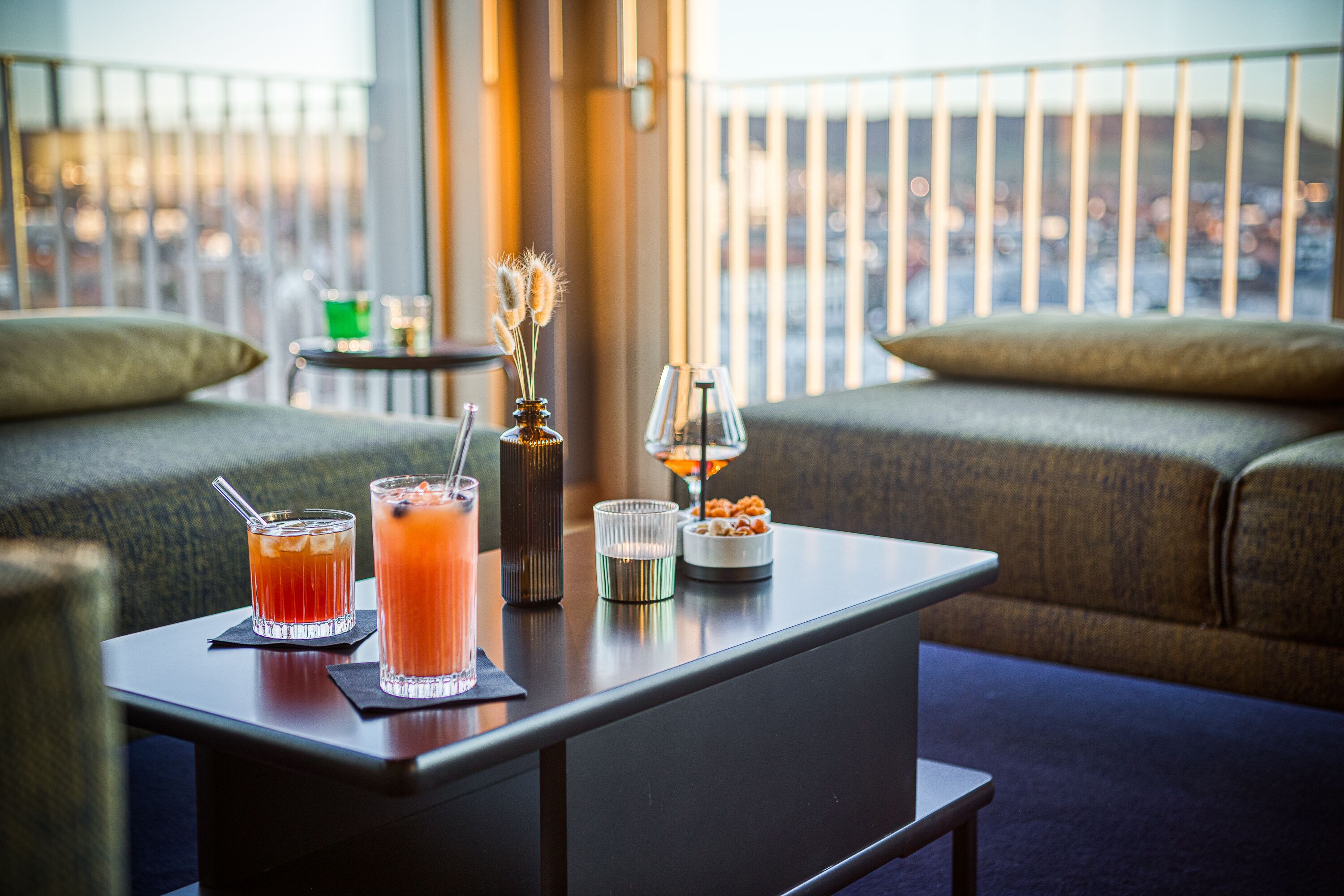 A bar area with two drinks, a candle, and a small dish of snacks on a table.