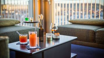 A bar area with two drinks, a candle, and a small dish of snacks on a table.