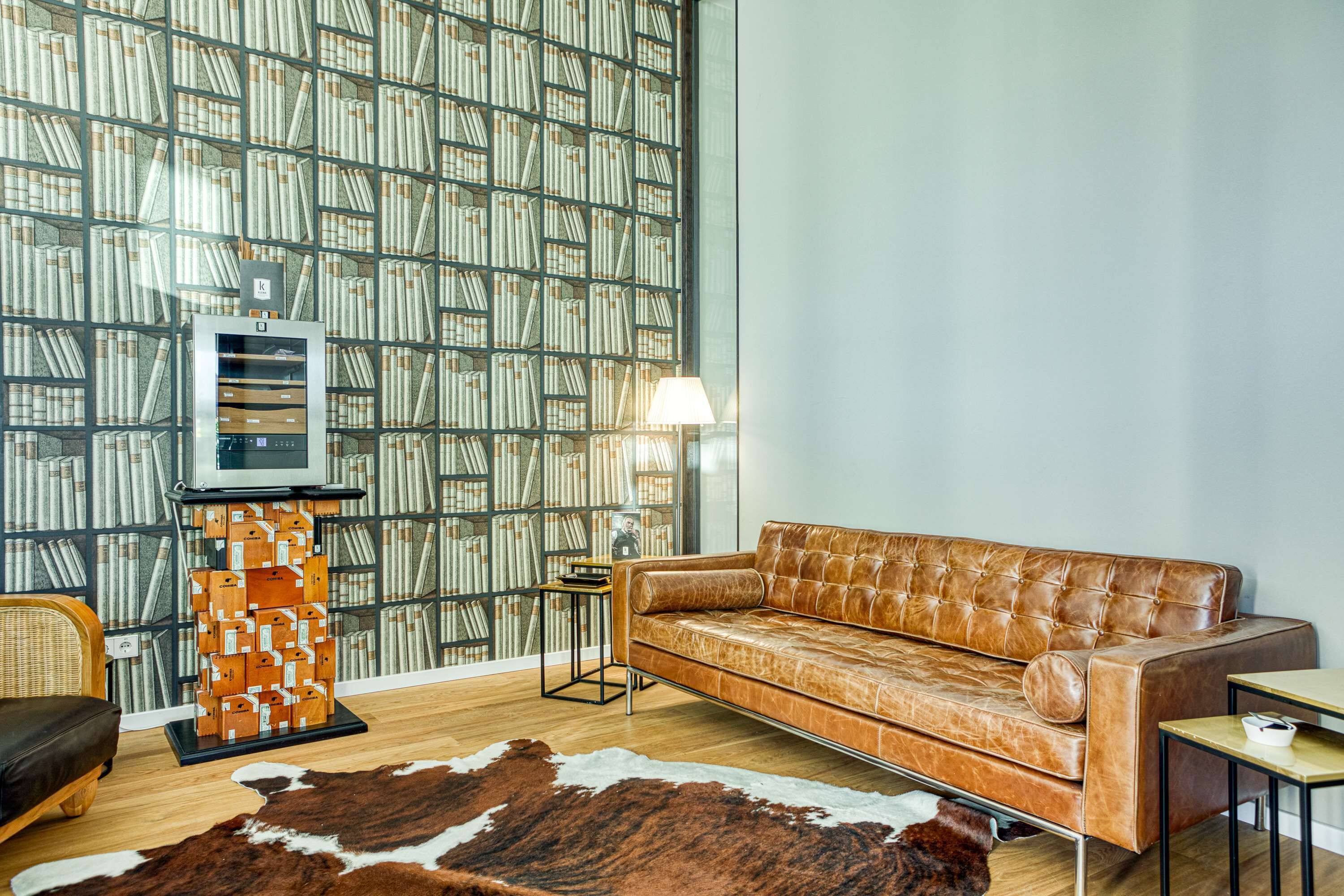 A modern living room with a leather sofa, a wooden bookshelf, a cowhide rug, and a lamp.