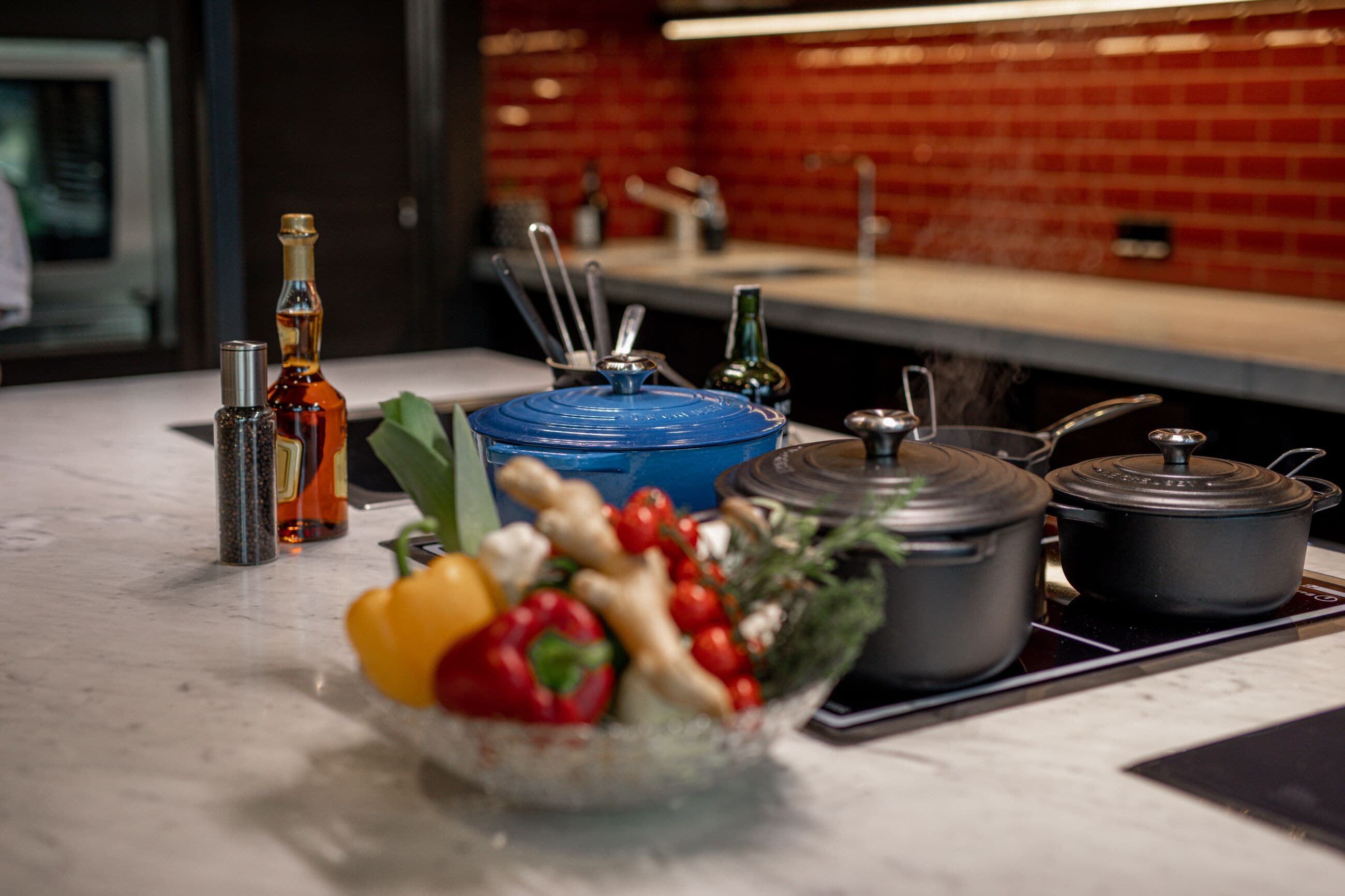 A kitchen counter with various cooking utensils, a bowl of vegetables, and pots.
